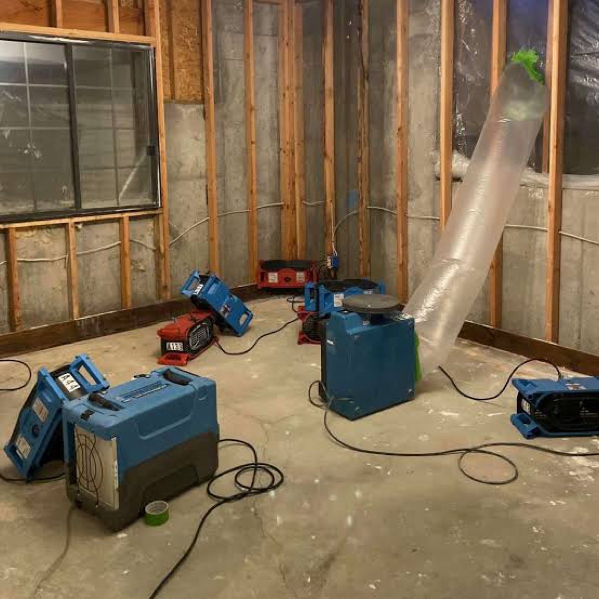 Air movers and dehumidifiers drying a room with walls opened to the studs after water damage – 77 Rapid Restore