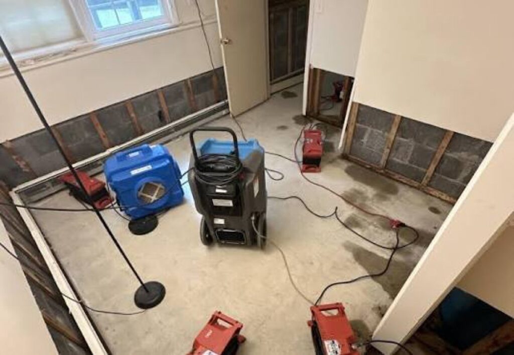 Dehumidifier, air scrubber and air movers drying a room with opened lower walls – 77 Rapid Restore